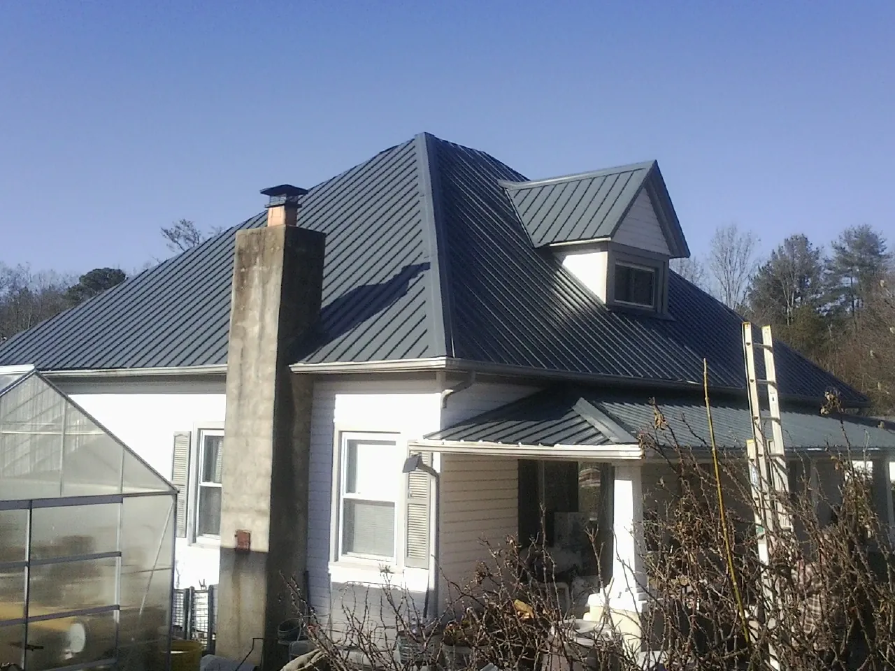 Dark blue standing seam metal roof on a white farmhouse with dormer — Slate & Tile Roof Repair by Roofing Brothers in Stoddard