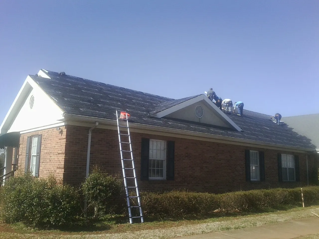 Crew tearing shingles off a brick ranch roof with a ladder set — Metal Roof Repair work by our crew in Stoddard