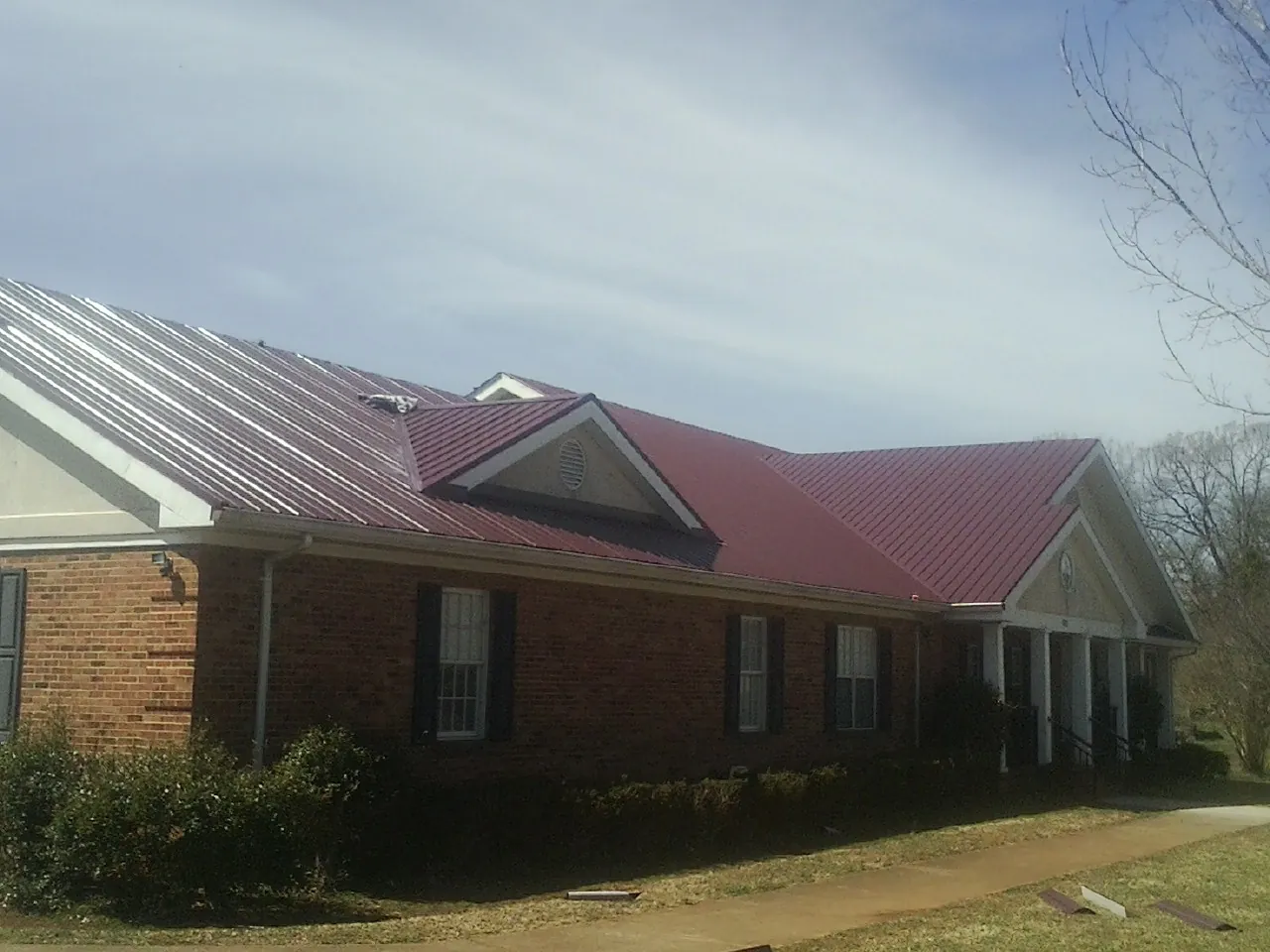 Red metal roof with gabled entries on a long brick building, from a Hail Damage Roof Repair job in Stoddard