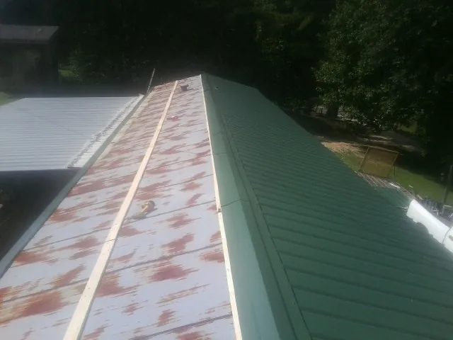 Old rusted panels beside newly installed green metal roofing — Wind Damage Roof Repair by Roofing Brothers in Stoddard