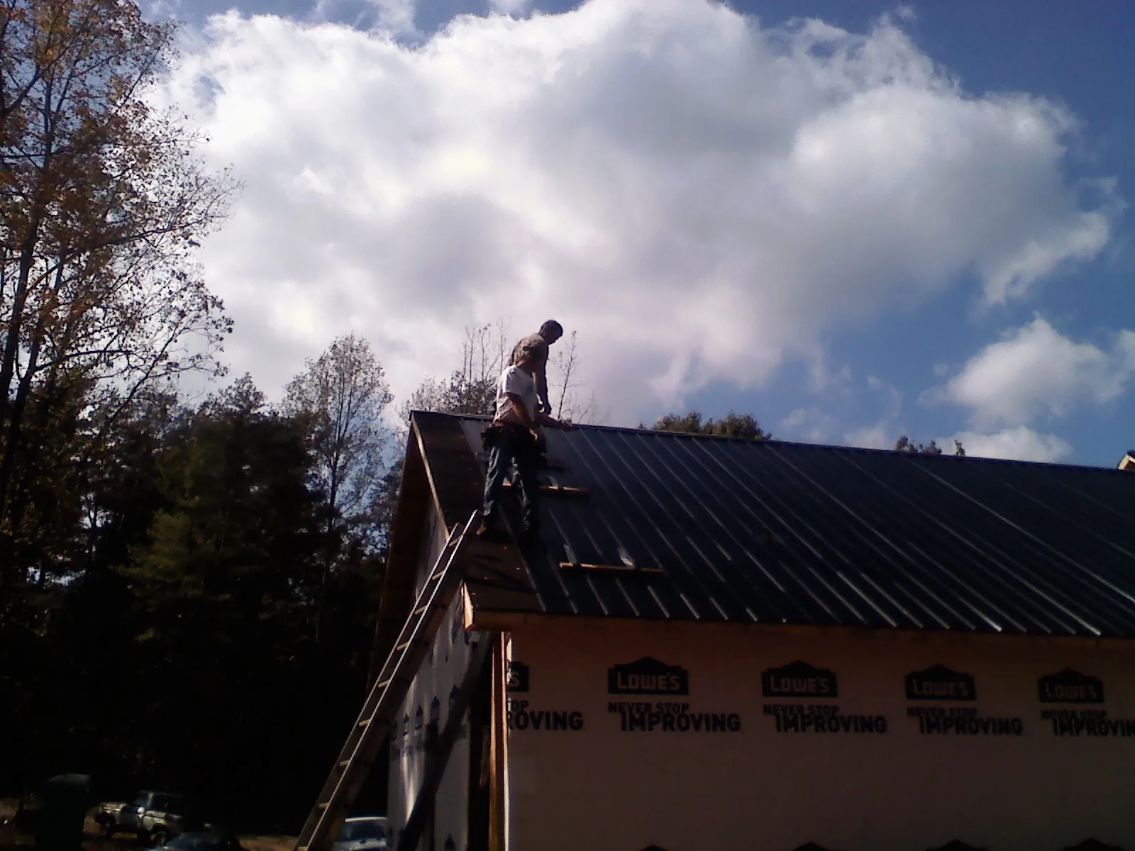 Roofer fastening dark metal panels high against a cloudy sky, from a Roof Inspection job in Stoddard