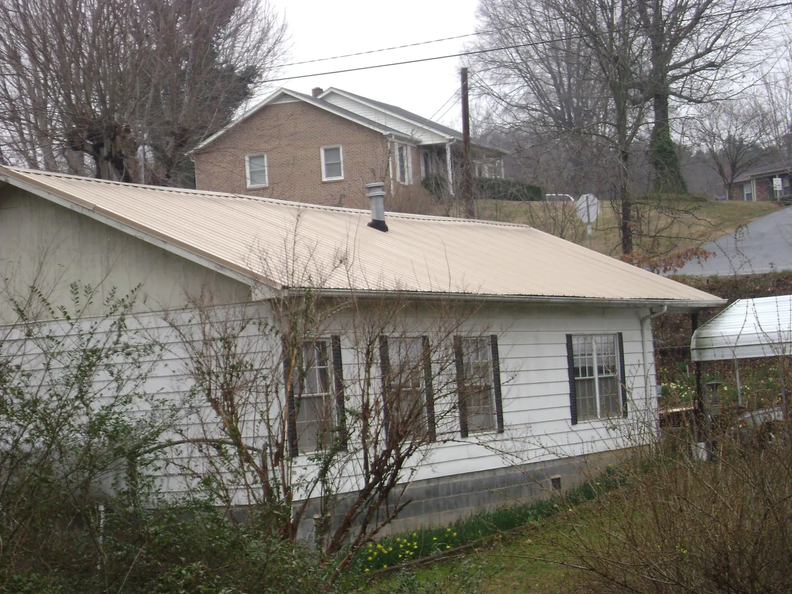 Tan metal roof on a white sided house set into a hillside — Commercial Roofing by Roofing Brothers in Stoddard