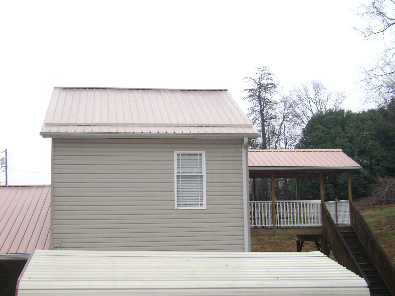Tan metal roofs on a two story addition and attached porch, from a Roof Replacement job in Stoddard